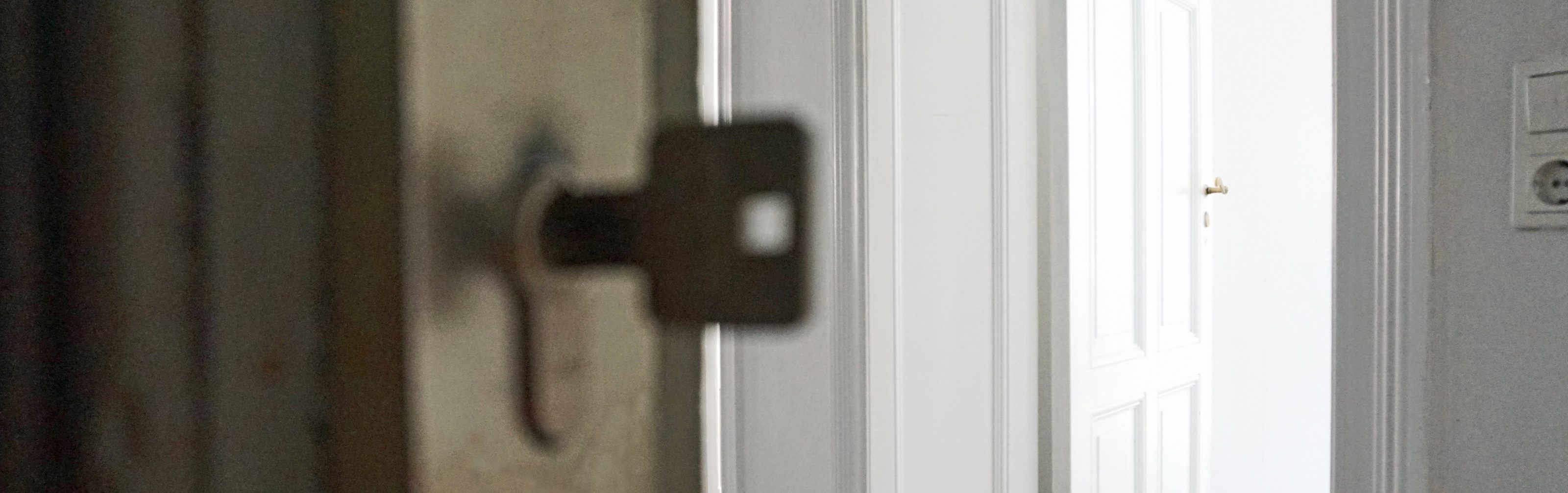 Durch eine offene Tür blickt man in eine leere Wohnung. Der Schlüssel zur Tür steckt im Schloss.