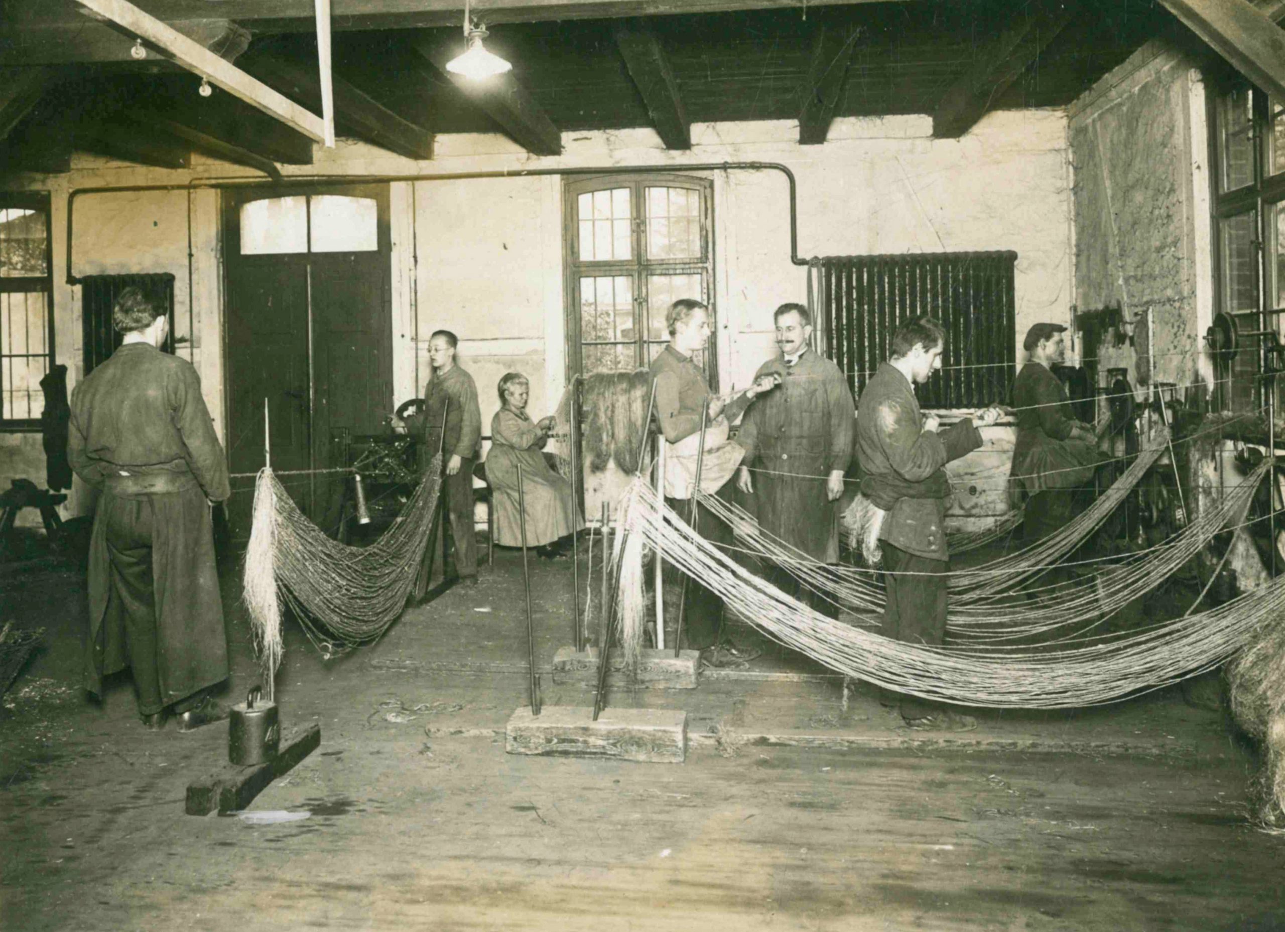 Sechs Männer und eine Frau befinden sich in einer Seilerei. Sie arbeiten. Das Bild stammt aus dem Jahr 1926.