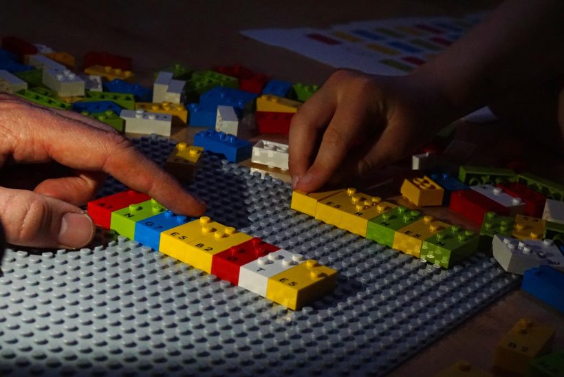 Zwei Hände fahren über Legosteine, die sich auf einer Platte befinden. Es handelt sich um Braille Bricks, Legosteine zum spielerischem Erlernen der Brailleschrift.