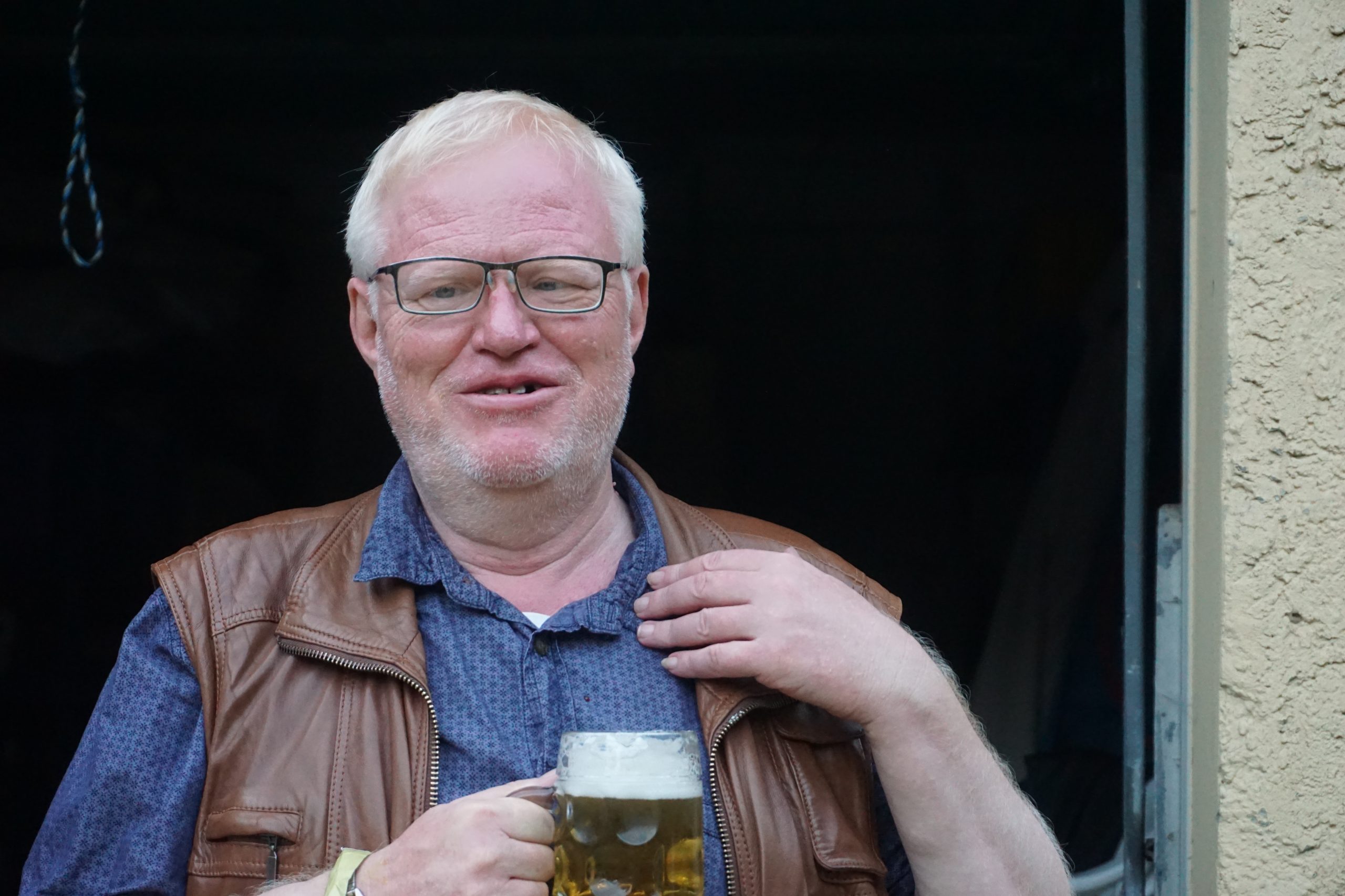 Ein Mann mit weißen Haaren lächelt und hält ein Bier in der Hand.