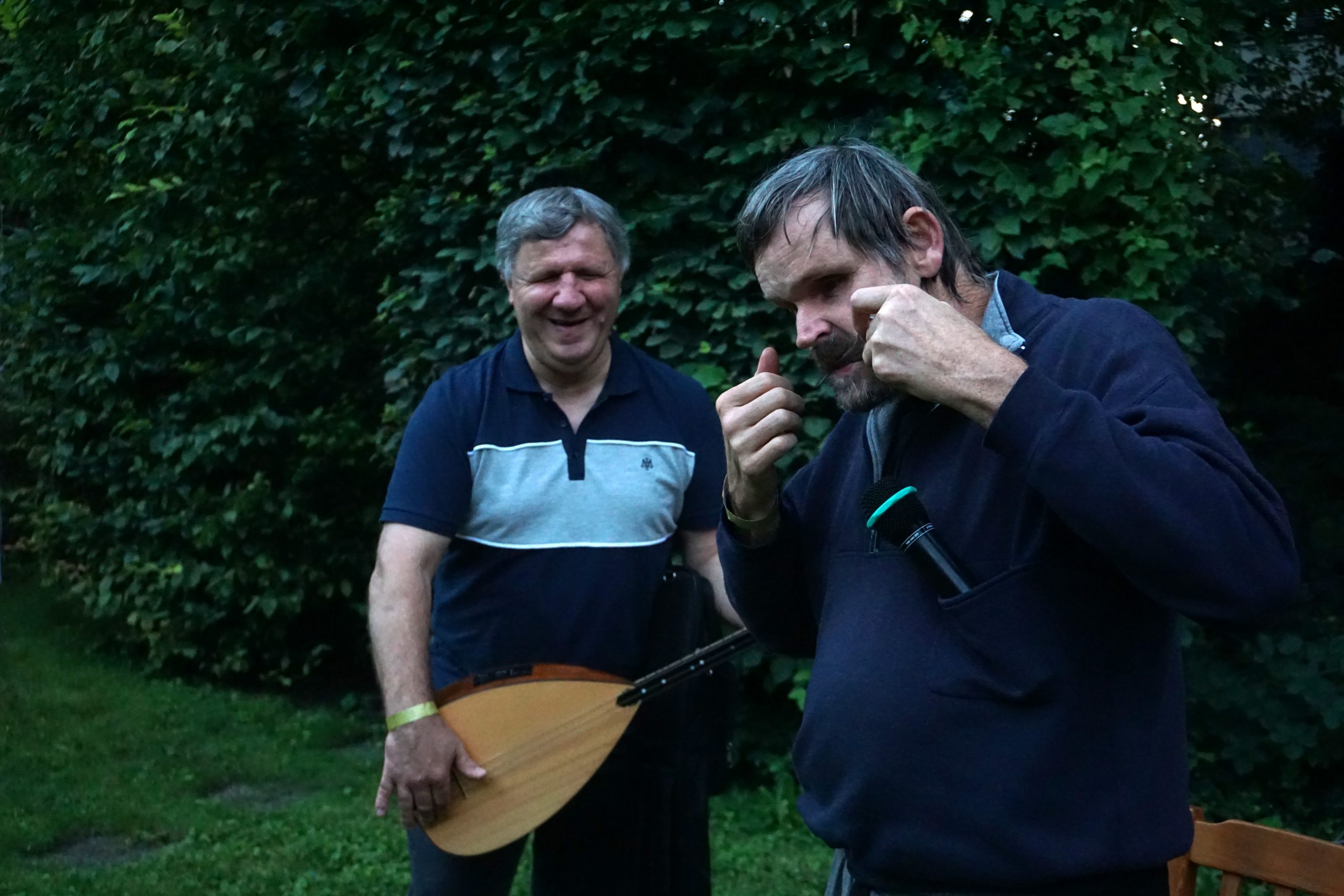 Ein Mann spielt ein türkisches Instrument, eine sogenannte Bağlama und lächelt. Neben ihm ist ein weiterer Mann, der eine Maultrommel spielt.