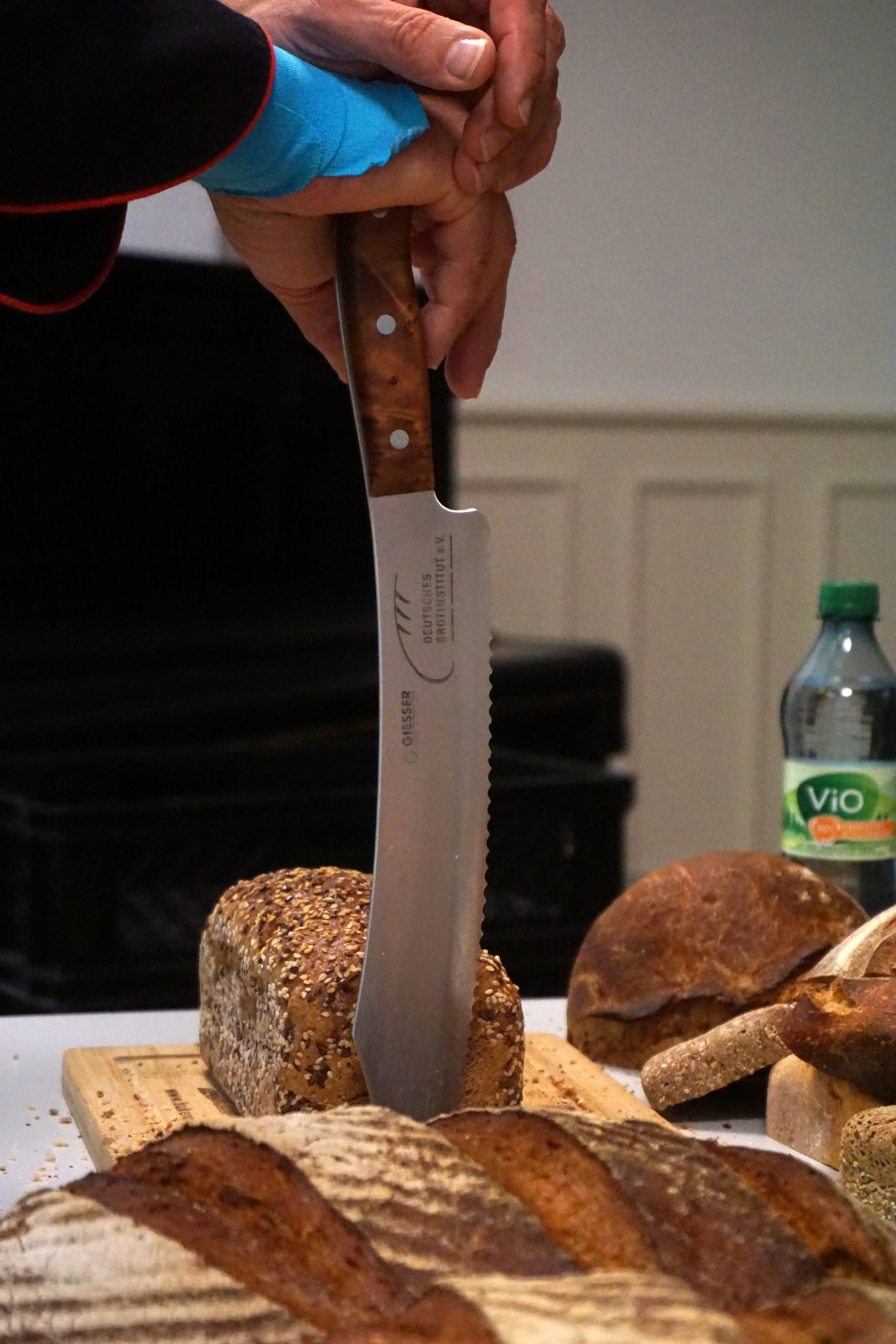 Ein Brotmesser wird auf ein Brotschneidebrett gestützt. Drum herum liegt Brot.