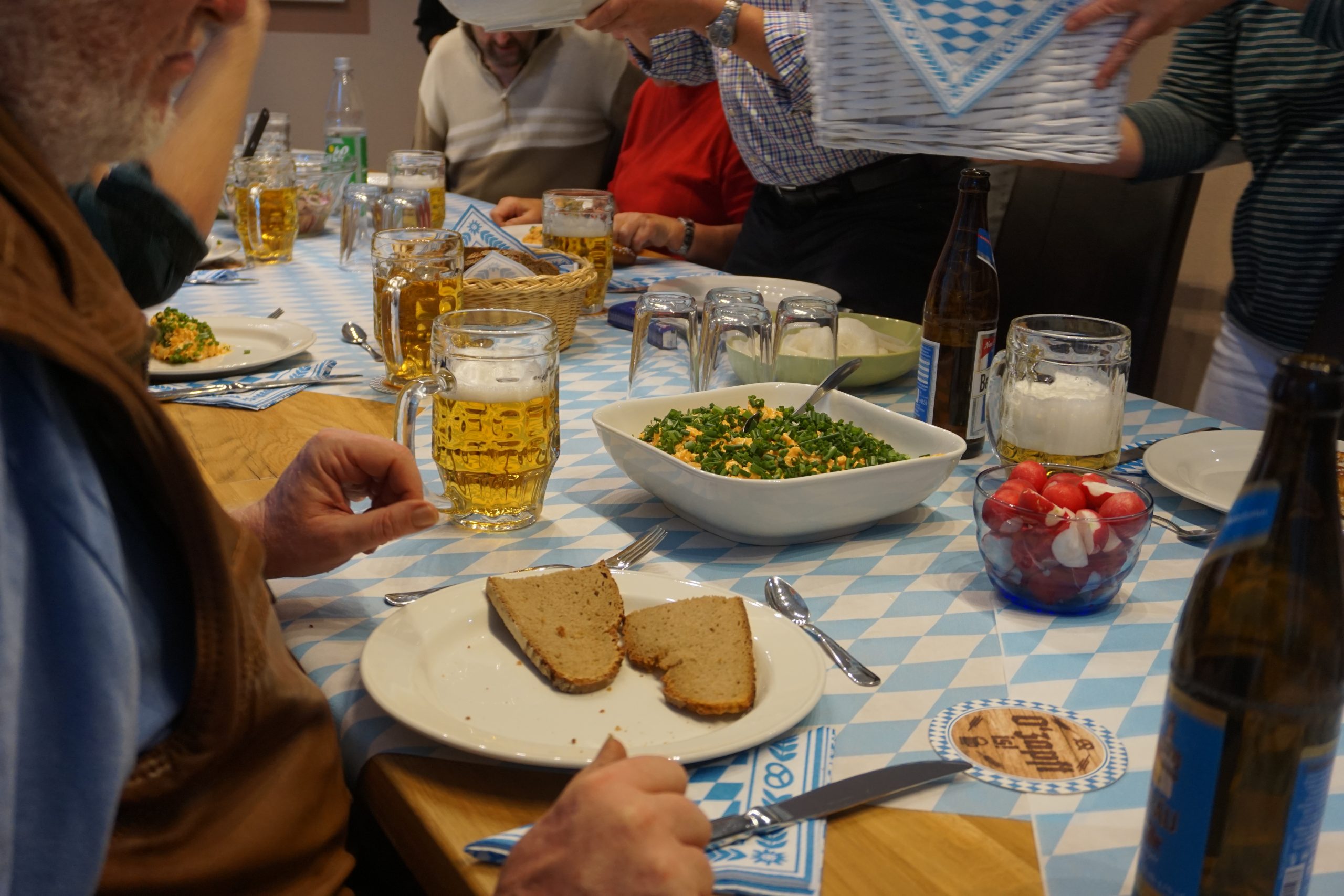 Ein gedeckter Tisch mit einer bayerischen Brotzeit. Mehrere Menschen sitzen an dem Tisch.