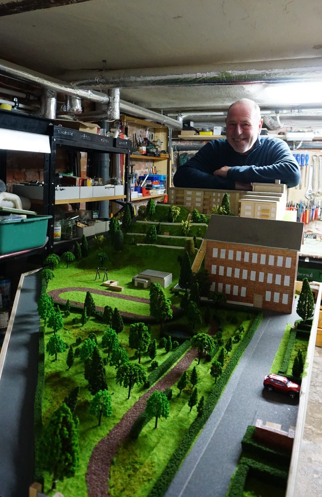 Ein Mann steht in einer Kellerwerkstatt hinter einem Geländemodell.