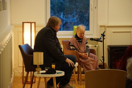Ein Herr sitzt im 90 Grad-Winkel zu einer älteren Dame und spricht mit ihr.