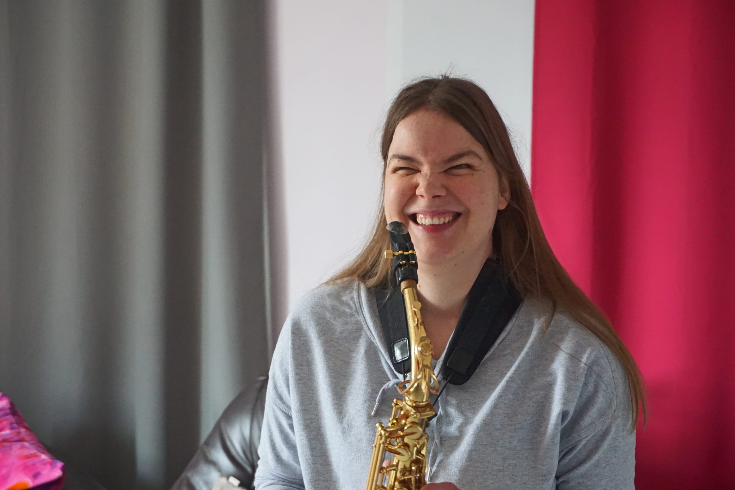 Eine Frau lacht. Sie hält in beiden Händen ein Saxophon. Das Mundstück befindet sich auf Mundhöhe.