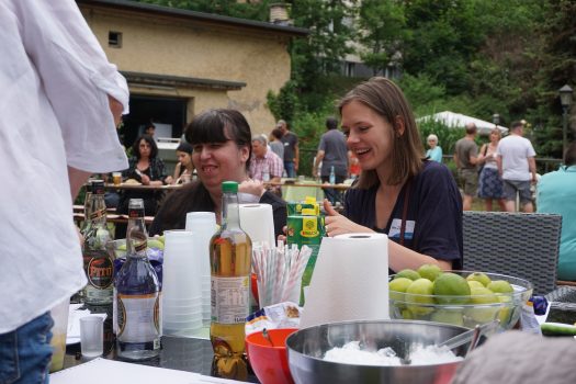 Zwei Frauen sitzen an einem Tisch und mixen Cocktails.