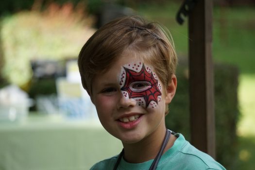 Ein Portraitbild eines Jungen, der schätzungsweise neun Jahre alt ist. Sein linkes Auge ist mit roter Spiderman-Optik geschmickt. Er lächelt.