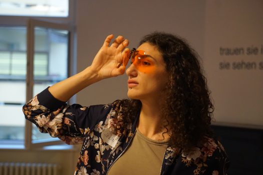 Eine junge Frau hält orange getönte Brillengläser vor ihre Augen.