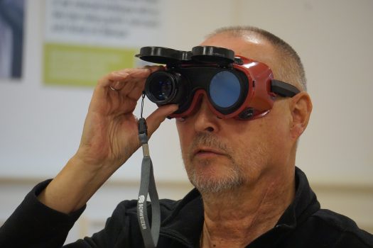Ein Mann mit Schweißerbrille schaut durch ein kleines Fernglas.
