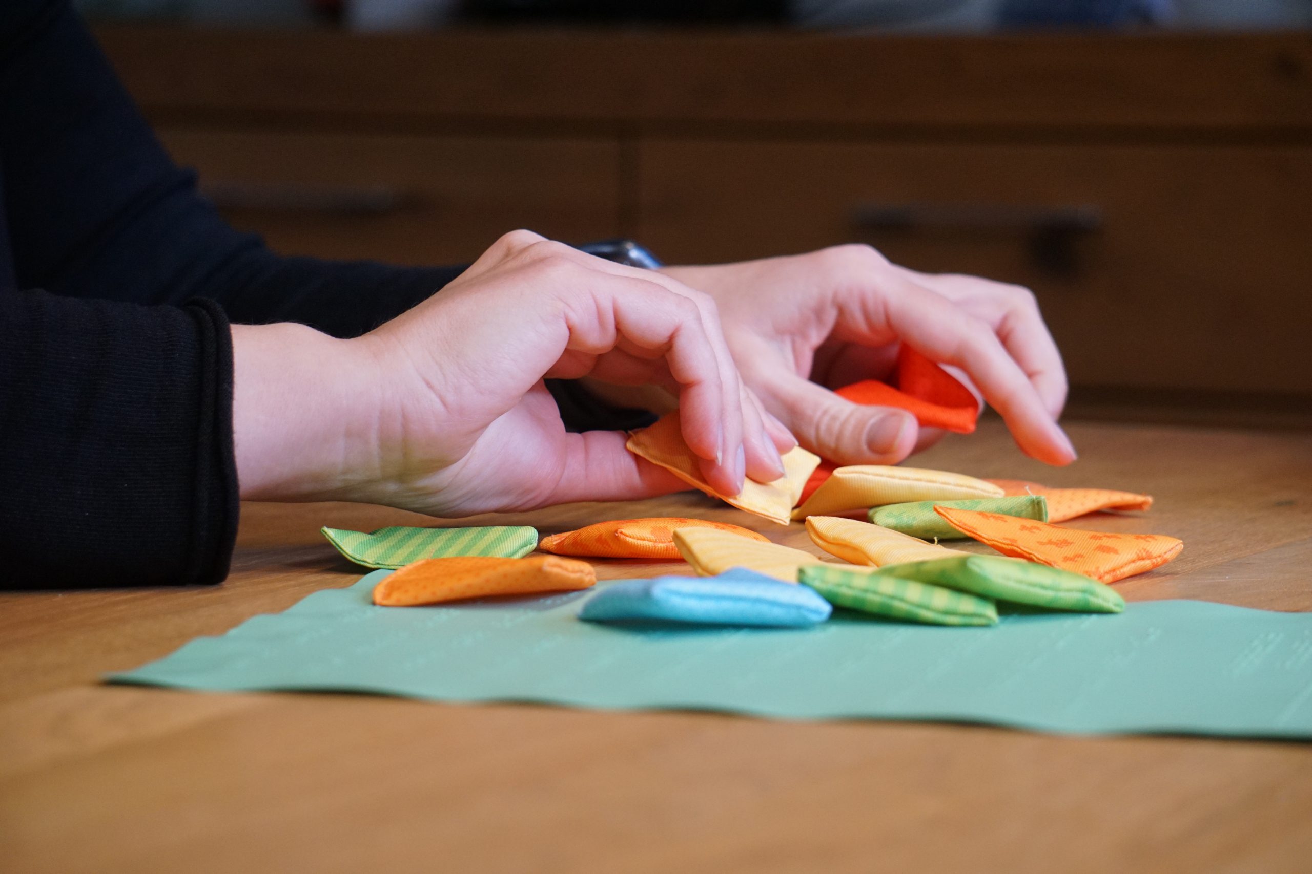 Zwei Hände erfühlen kleine unterschiedlich farbige und gemusterte Stoffkissen, die auf einem Tisch liegen.